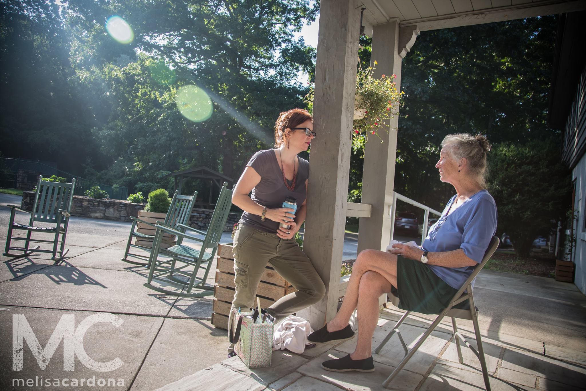 Two women of different generations sit on a porch talking to each other, the morning sun warms them from behind